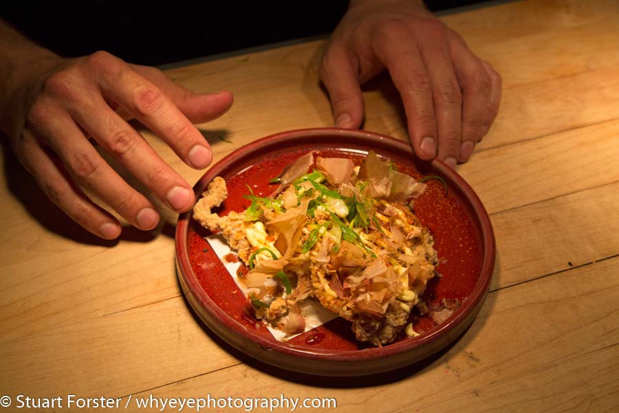 The hands of Chef Darren Maclean placing a plate of Japanese cuisine on the counter top of Shokunin in Calgary.