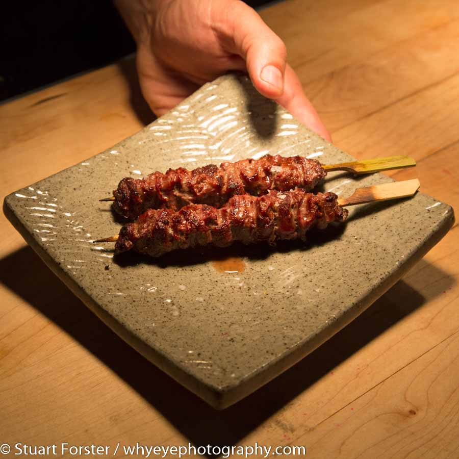 The hand of chef Darren MacLean presents a plate of skewered grilled meat at his Shokunin restaurant in Calgary, Alberta