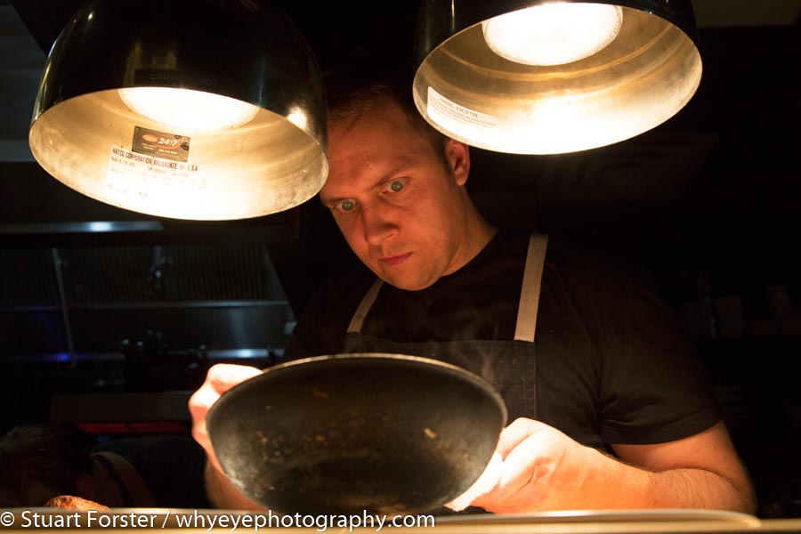 Darren MacLean spooning ingredients from a pan next to counter lights while working in the kitchen at Shokunin in Calgary.
