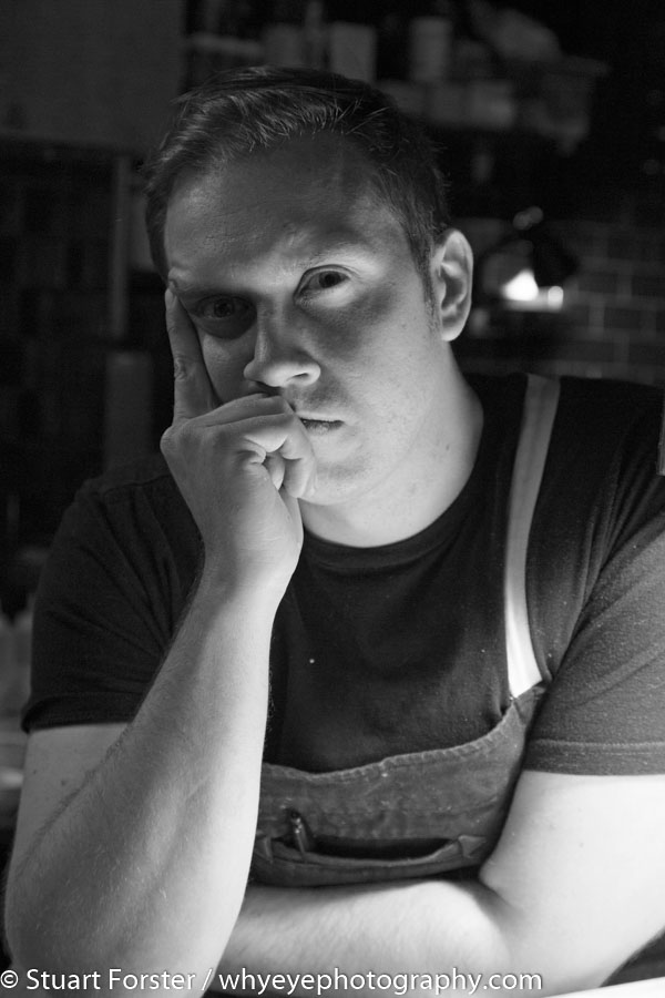 Black and white image of Chef Darren MacLean at Shokunin, Calgary, looking out from the kitchen in a moody pose.