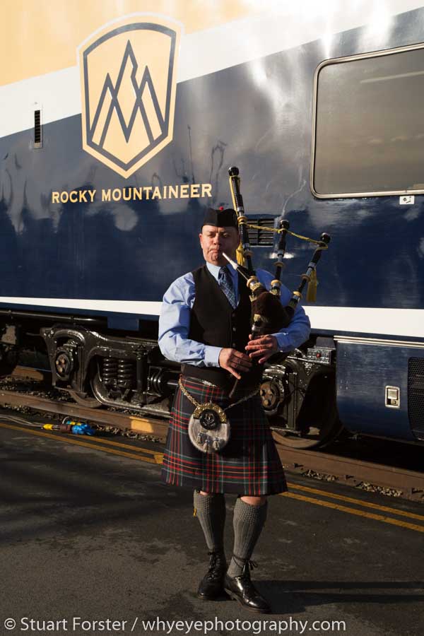 Kilted bagpiper in front of the Rocky Mountaineer logo while the luxury train is at its station in Vancouver, British Columbia.