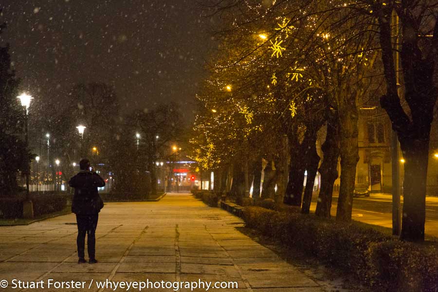 A woman photographs the snow falling on a city centre street at night in Riga, Latvia