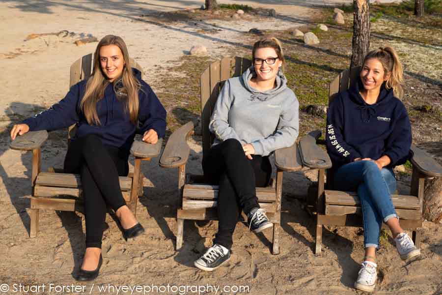 Jordan, Trinity and Driane seated in adirondack chairs outside of Gangler's Lodge in Manitoba, Canada.