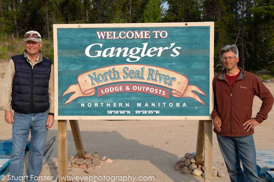 John Tronrud and Dr Brian Kotak at a sign for Gangler's North Seal River Lodge in northern Manitoba, Canada.