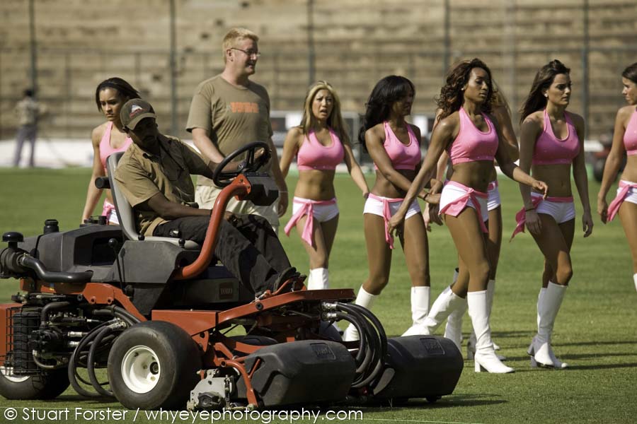 A groundsman trims the grass of the outfield at the M. Chinnaswamy Stadium while cheerleaders go through their routine.