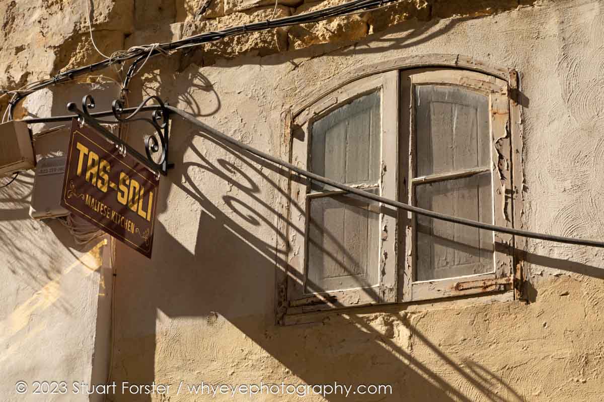 The sign of the Tas-Soli restaurant, where traditional Maltese cuisine is served, throws a shadow across the wall and window in Archbishop Street, Valletta.