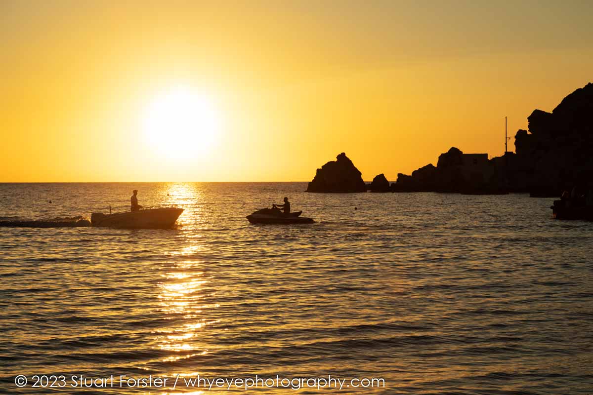 A boat and jet ski on the water at Golden Bay, a popular spot for enjoying sunsets and travel photography in Malta.