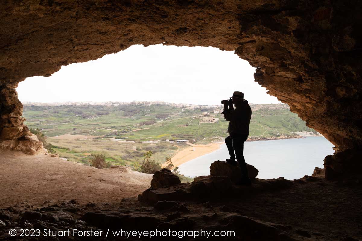 A photographer photographing Ramla Bay on Gozo, framed by the mouth of Tal-Mixta Cave.